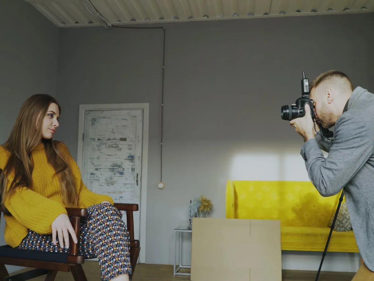 Fotograaf maakt een portret van een zittende vrouw in een lichte ruimte met daglicht door het raam