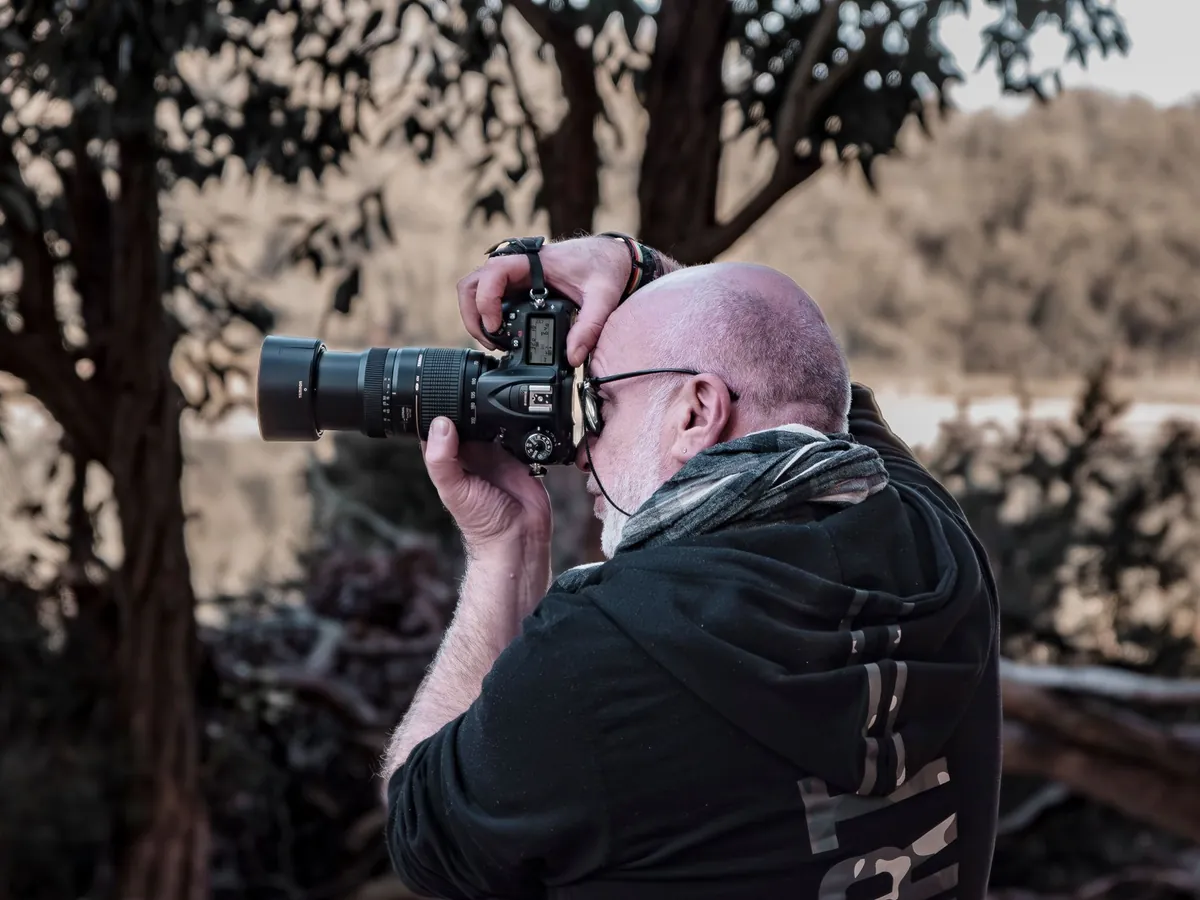 Fotograaf met een spiegelreflexcamera en een lang teleobjectief aan het werk tussen de bomen
