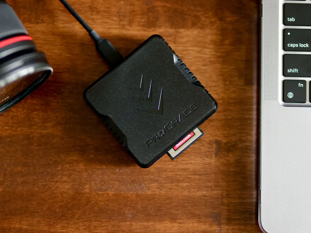 Zwarte kaartlezer met geheugenkaart naast een laptop op een houten tafel
