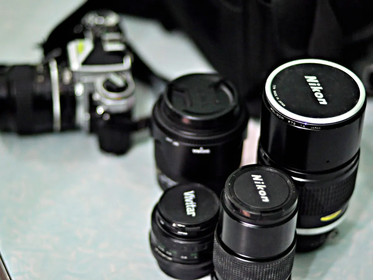 Oude handmatige objectieven en een analoge camera op een tafel, met Nikon-objectiefdoppen