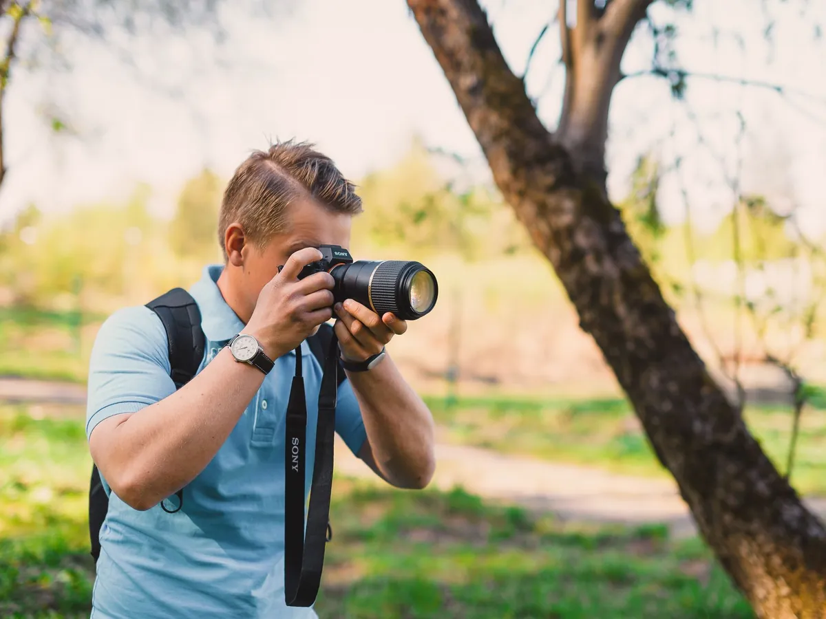 Man met rugzak fotografeert met een spiegelreflexcamera in een zonnig park
