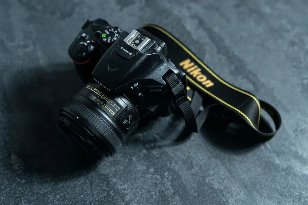 Nikon spiegelreflexcamera met objectief en draagriem op een grijze stenen ondergrond