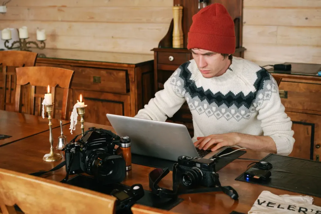 Man werkt op een laptop aan een houten tafel waarop meerdere camera's liggen