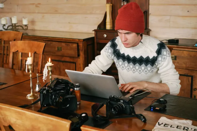 Man werkt op een laptop aan een houten tafel waarop meerdere camera's liggen