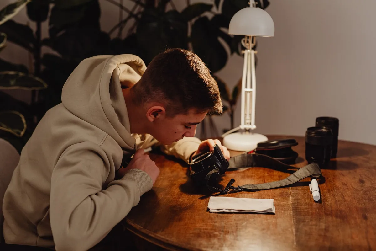 Jongeman bekijkt een spiegelreflexcamera van dichtbij aan een houten tafel